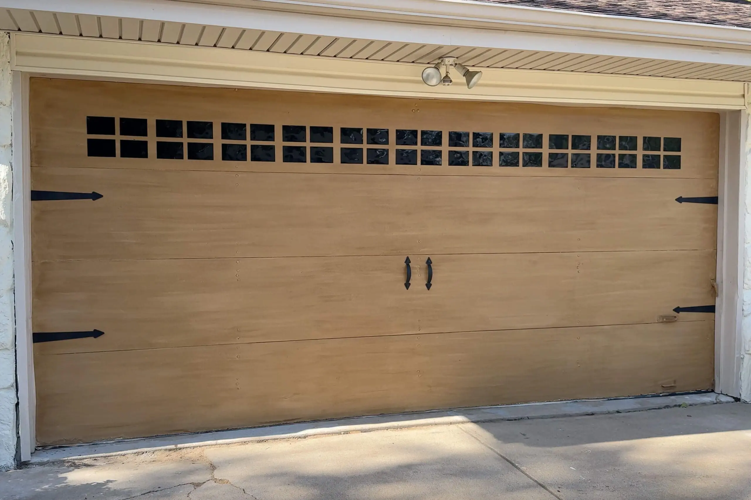 Completed faux wood garage door makeover featuring a smooth wood-toned finish with black decorative hardware and faux window panels at the top for a carriage-style look.